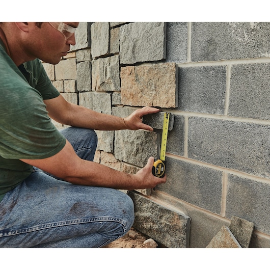 25 foot FATMAX classic tape measure being used by a person to measure brick tile length outside.