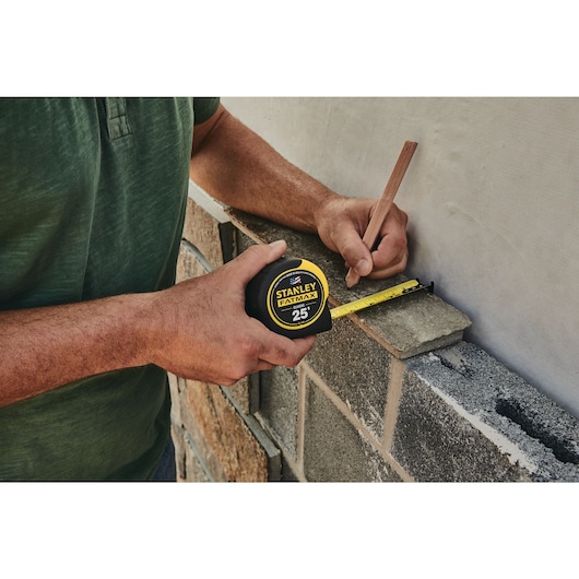 25 foot FATMAX classic tape measure being used by a person to measure width of a tile outside.