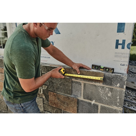 25 foot FATMAX classic tape measure being used by a person to measure brick tile length.