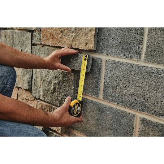 25 foot FATMAX classic tape measure being used by a person to measure brick length.