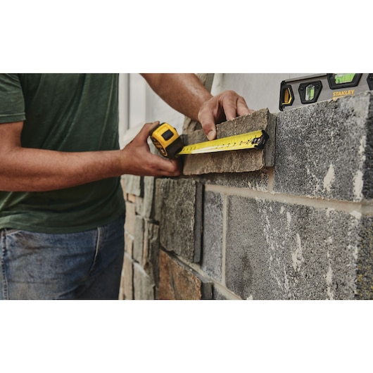 25 foot FATMAX classic tape measure being used by a person to measure brick tile length.