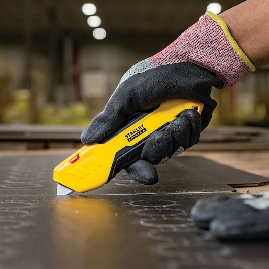 Fatmax auto retract squeeze safety knife being used to cut a sheet.